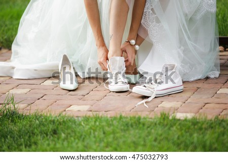 Bride change shoes sneakers. Bride dressed in long wedding dress.