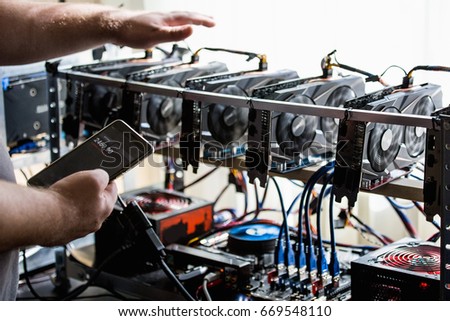 A man holds a phone with a bitcoin exchange and checks the temperature of the computer with graphic cards