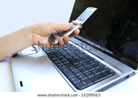 Hand holding mobile cell phone in front of laptop