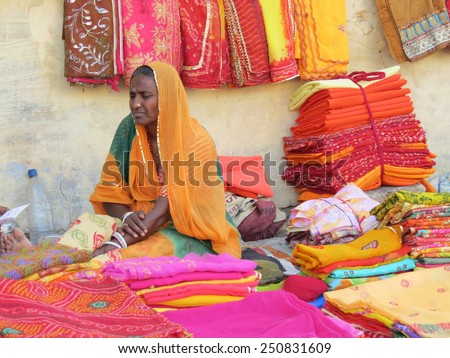 Jodhpur, India - April 1st, 2013: Indian woman selling brightly coloured saris from her pitch on the pavement. Many people sell their wares this way and the authorities seem to be okay about it.