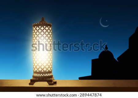 An illuminated ramadan lantern against blue night sky with an crescent moon.