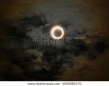 solar eclipse with clouds, moon passing directly in front of the sun to create a ring of fire