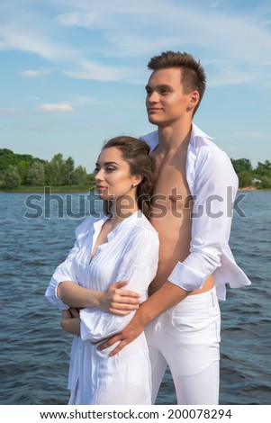 Man hugging woman in white dress near a water