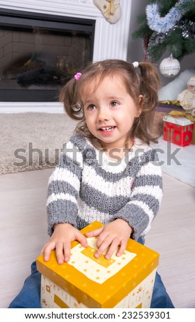 Child under the Christmas tree near the fireplace opens gift. Little girl with open box with a gift near the Christmas tree