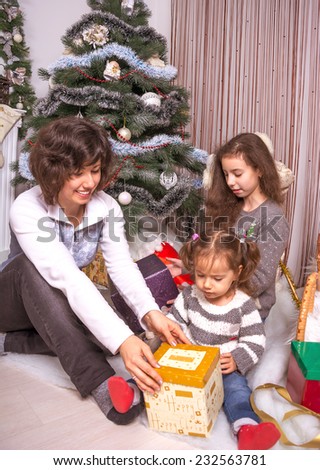 Family with gifts near a Christmas tree. Mom with kids opening presents under the Christmas tree