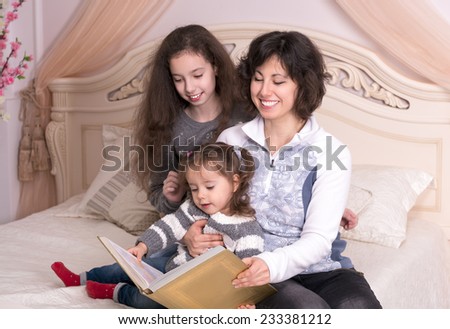 Mom reading a book with children. Little girl holding a big book