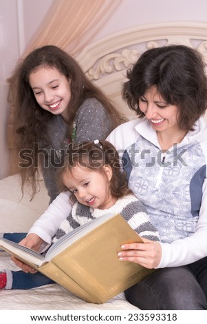 Mom reading a book with children. Little girl holding a big book
