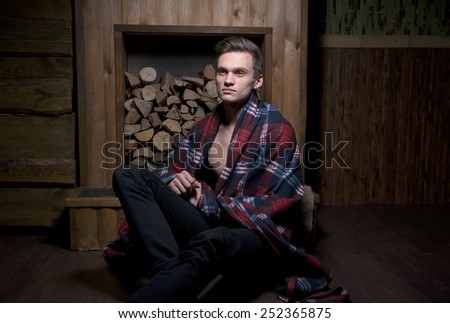 Man wrapped in a blanket in the rural interior in front of a stack of wood