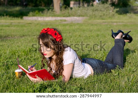Young girl with a notepad pen and a cup of coffee in a summer park on the grass