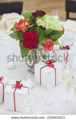 Glass Vase Full of Bright Flowers Surrounded by Presents as Table Centerpiece - Narrow Focus