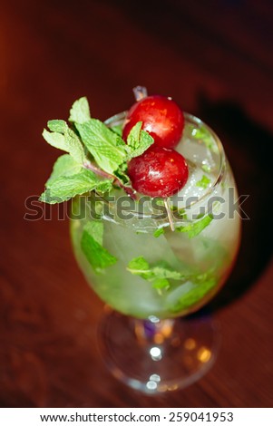beautiful frozen cocktail glass with ice, mint and grape on a dark wooden bar counter
