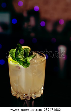 beautiful frozen cocktail glass with ice, mint and pineapple on a dark wooden bar counter, bokeh bright background