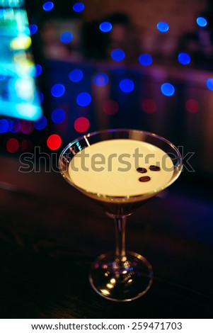 beautiful  brown cocktail in martini glass with coffee and white foam on a dark wooden bar counter, bokeh bright background