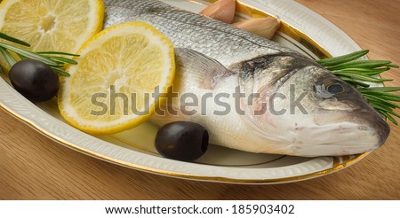 Sea bass with lemon, garlic, lemon and rosemary on the wooden background