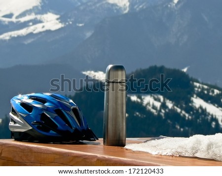 Bike helmet and vacuum flask in mountains in nice winter weather with snow