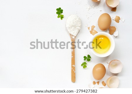 Broken eggs and flour in wooden spoon on white background, baking background.