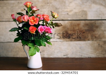 bouquet of beautiful roses in a enamel vase on rustic wooden background