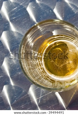 Glass of beer with edges outside center seen from above on metallic table