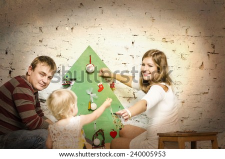 Happy family of mother father and baby sitting together on sofa and looking on wooden new year tree and decorating a Christmas tree.