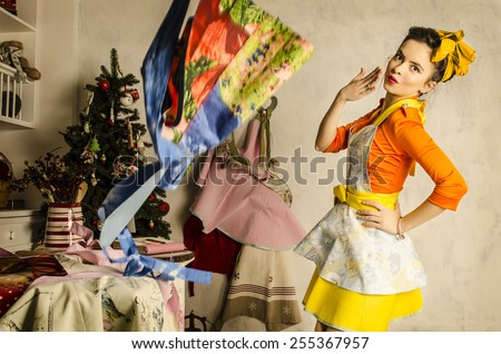 Beautiful and dressed up woman in kitchen with kitchen tools standing and smiling. America 60-s pin-up style.