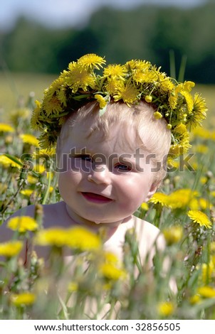 Boy with diadem from dandelions seating in spring flowers