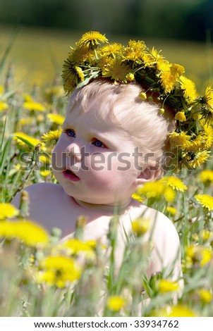 Boy with diadem from dandelions seating in spring flowers