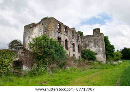 Ruined house in grassy field with blue sky and white clouds