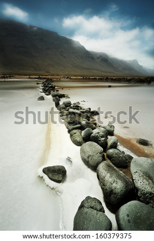 salt on a sunny day with high clouds with mountains in the background and rocks in the foreground row in Lanzarote, Canary Islands (Spain)
