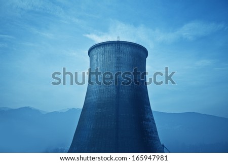 Huge chimney rises up in an industrial zone near mountains.