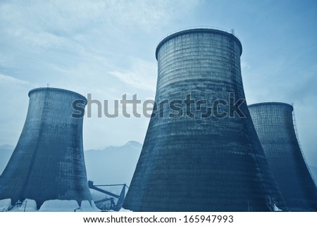 Huge chimneys rise up in an industrial zone near mountains.