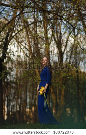 Girl in blue dress with yellow flowers stands alone in the park. Outdoor photography.