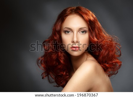 Portrait of a young ginger woman on a dark background. Low key. Long Curly Red Hair.