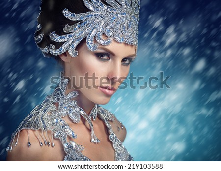 Winter beauty woman in a shiny dress . Christmas girl makeup. Holiday Make-up. Snow Queen High Fashion Portrait over Blue Snow Background.