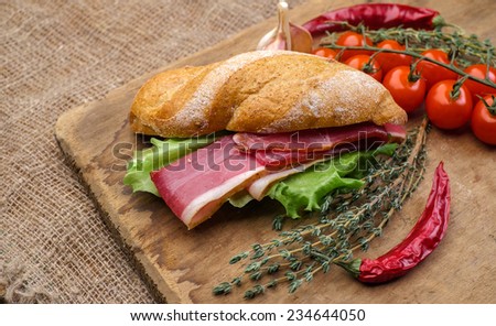 Sandwich on a wooden cutting board with slices of bacon and lettuce. Cherry tomatoes and thyme.