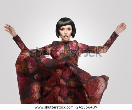 Fashion portrait of a beautiful girl in a flying dress. Model in a red dress with flowers on a gray background.