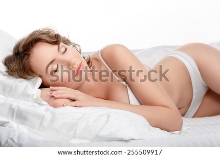 Sexy young woman is sleeping in her bed. Girl in lingerie on the bed. Sexy brunette on white bed sheets. The morning sun in the bedroom.