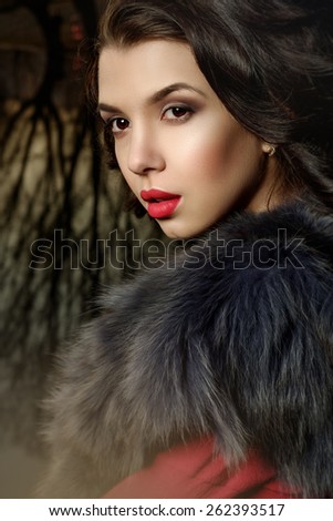 Portrait of Beautiful girl in the park. Red dress with a fur collar. Red lips fashion makeup. Portrait Outdoors