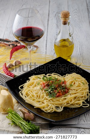 Italian pasta cooked in a rustic style with a sauce of fresh tomatoes and garlic on a wooden table with a glass of red wine.