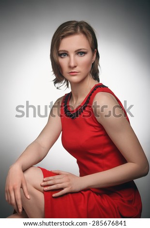 Young elegant woman in red dress sitting on chair, studio shooting. Looking at camera.