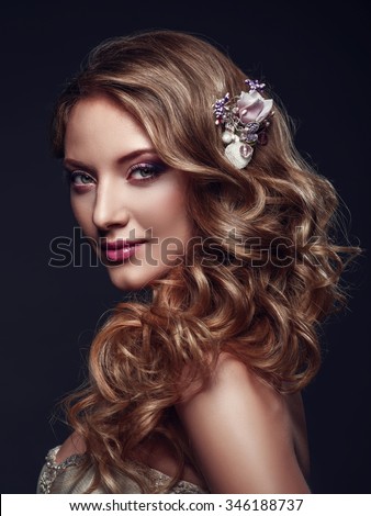 Beautiful woman with evening make-up and long wavy hair. Bright makeup. Fashion photoshoot. Bride half-turned. Studio shoot on a grey background.