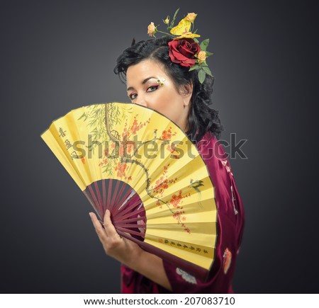 Caucasian kimono woman with flowers in her hair holding traditional fan on gradient background