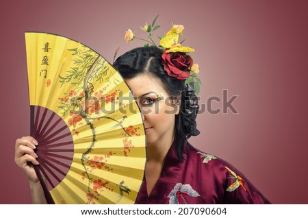Kimono woman hiding the right side of face behind Asian fan on gradient background