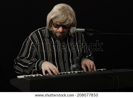 Middle aged bearded musician improvising and writing music with digital piano on black background