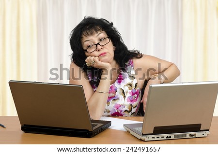 Mature woman is boring on webinar on front of two laptops