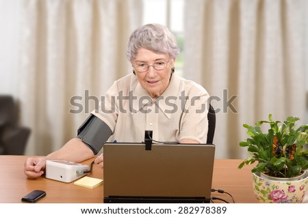 Old grey haired woman demonstrates how easy to monitor her blood pressure and pulse at home. All her vital signs are transmitted to telemedicine center, at the same time