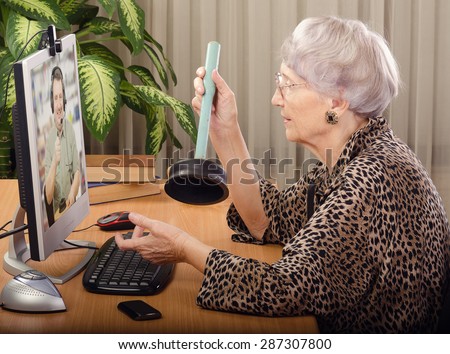 Senior woman is clearing how to fix a clogged toilet. She sits on front of computer monitor and asks to virtual plumber. On the screen, plumbing expert explains how to use a plunger toilet.