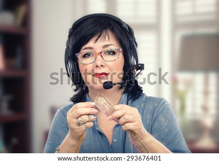 Portrait of adult student learning knitting by on-line lesson. Black haired woman in headset knitting with wooden needles. She looking at camera