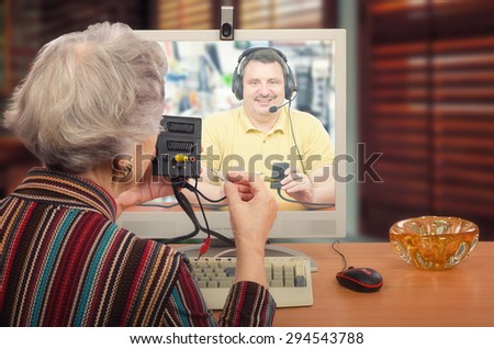 Old woman is being taught by on-line video chat. Professional from technical support service explains how to install audio-video adapter.