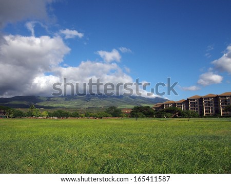 Grass field in a Park in Kaanapali on Maui, Hawaii next to a hotel with Mountains and clouds in the distance.