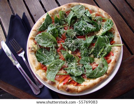 Spinach Margarita Pizza with a fork and knife on top of a napkin on an outdoor table.